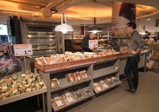 Casper helpt een klant bij de broodafdeling. Achter hem een ruime oven om vers brood in af te bakken.