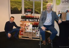 Ramon van Huffelen hurkt neer naast een deel van het aanbod uit het Organic Wine Concept. Aan tafel zit zijn vader Otto. Ramon vertelt dat zo'n 60 natuurvoedingwinkels gebruik maken van het Organic Wine Concept.