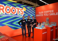 De stand van Neuteboom Coffeeroasters knalt van het beeldscherm, het kleurrijke merk Roots gaat als het aan Jan Hart ligt breder de markt op. "Na twee jaar exclusief bij PLUS te hebben gestaan, is Roots vanaf nu breed beschikbaar." Naast Jan staan Michelle Teijgeler en Gilbert Willemsen.